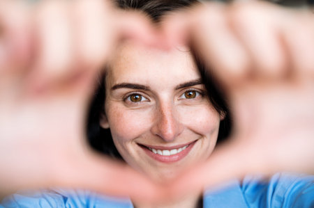 Selective focus on smiling woman face. Happy female making heart love hand gesture sign. Having fun,...