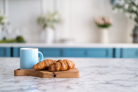 Wooden kitchen board with croissants and blue coffee mug on stone marble table top. Blurred abstract background from interior. Concepts of tasty breakfast, copy space.の写真素材
