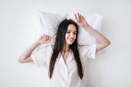 Top view of young woman in home sleepwear lying on memory foam pillow, looking at camera with smile. Female rest on hypoallergenic cushion. Model isolated on white background. Good mood in the morningの写真素材