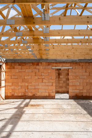 Example of new unfinished house under construction with wooden roof beams over brick walls with large windows and cement screed or concrete foundation on floor in living space, vertical shotの写真素材