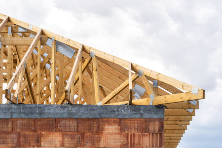 House development. Building under construction. Roof installation with wooden boards on rooftop. Timber frame on attic with metal joints on top against copy space sky on backgroundの写真素材