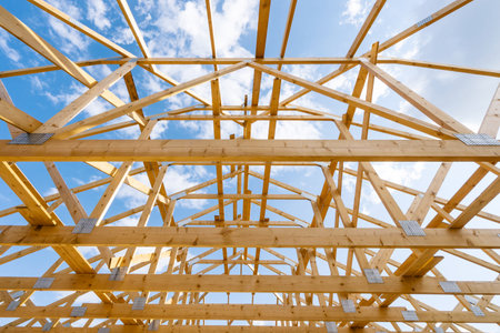 Renovation, remodeling concepts. Low angle view of unfinished attic space with wooden framework construction against blue sky background. Beams, lumbers and joint planks on rooftop installationの写真素材