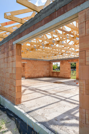 Vertical shot of new family brick house with concrete foundation and cement screed on the floor under wooden roof frame. Concept of construction site, building process, unfinished homeの写真素材