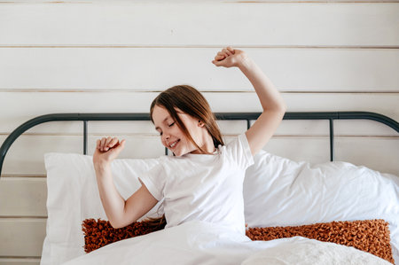 Portrait of happy smiling kid waking up and stretching in comfortable bed in cozy bedroom. Child enjoying perfect morning after good sleep at home.の写真素材