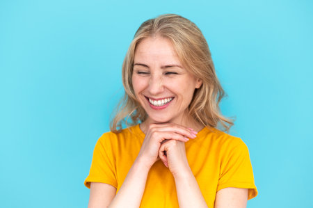 Happy cheerful young woman rejoicing at positive news or birthday gift, standing with closed eyes isolated on blue copy space background with joyful and charming smileの写真素材