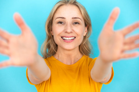 Positive smiling woman on blue background reaching for the camera with hands. Wanting to embrace, hug. Invite, greeting concept. Come into arms.の写真素材
