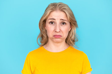 Portrait of sad and frustrated woman with upset face looking at camera, pouted her lips, ready to cry, isolated on blue background. Concept of misunderstanding, problems, disappointed and dissatisfiedの写真素材
