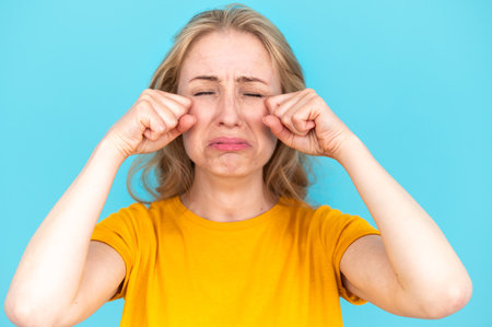 Studio portrait of crying upset woman isolated on blue background. Sad young female feeling lonely, unhappy. thinking about problems, suffering from bad relationship, break up or divorceの写真素材