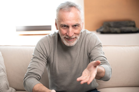 portrait of mature man sitting on sofa and talking with friend by video call. positive middle aged...