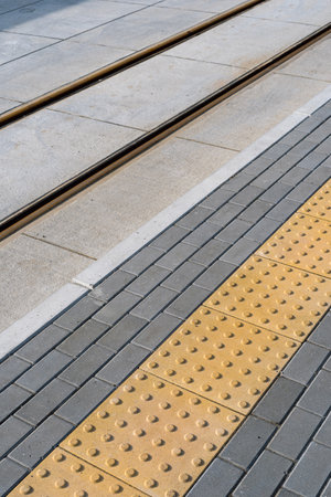 Pavement sidewalk with tactile slab for helping blind people on road near tram rails at modern city. Warning sign. Safety concept. Accessible environment for disabilitiesの写真素材