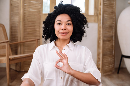 Portrait of smiling african american woman showing ok gesture. Female doing yoga exercise in room...