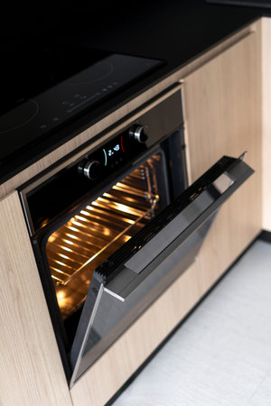 Element of glass ceramic induction stove over electric oven with open door. High angle view with built in appliance. Vertical shot of household equipment in kitchen spaceの写真素材