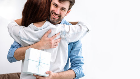 Loving smiling husband hug his wife, feeling thankful for getting present in gift box. Happy young couple embracing, celebrating marriage anniversary or happy birthday. Copy space, web banner viewの写真素材