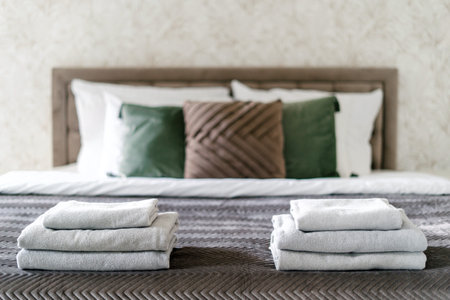 Selective focus on clean bath towels neatly folded on comfort double bed with pillows and blanket in cozy hotel room. Detail in interior. Rest and relax concept. Contemporary bedroomの写真素材