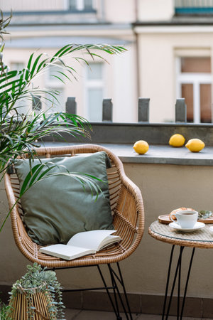 Vertical shot of rattan armchair with green cushion and diary journal or paper book for reading next to coffee table with cup on terrace of cafe in city center. Place for relax and having breakfastの写真素材
