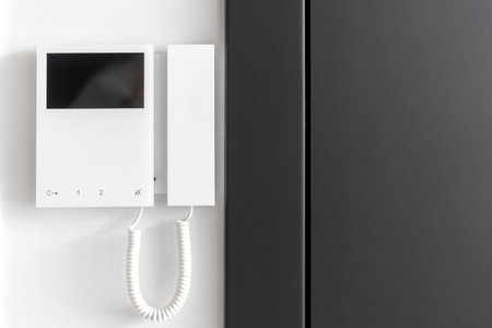 Close up view of electronic doorbell with buttons and copy space display on white wall. Black metal...