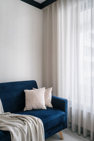 Detail in interior of living room, modern blue couch, soft plaid and decorative cushions near window...