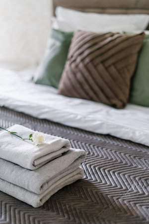 Closeup of clean terry towels decorated with rose flower and folded on comfort bed in hotel room...