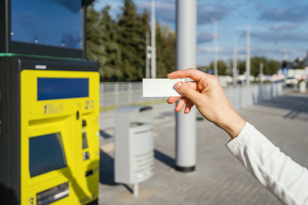 Selective focus on paper ticket in female hand against blurred atm, bus station public transport background. Copy space. Woman showing travel pass.の写真素材