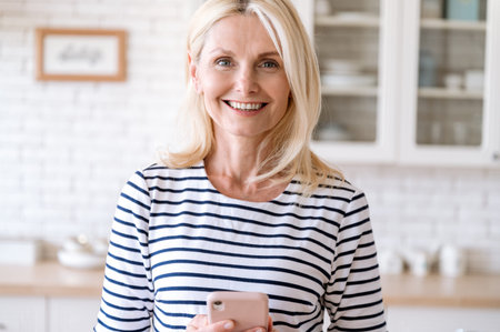 Portrait of smiling happy mature woman holding modern cellphone in hands. Female waiting for call,...