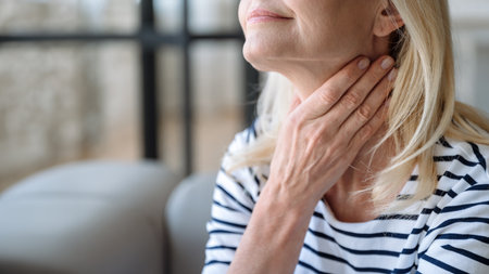 Selective focus on mature woman hand touching neck, having discomfort or painful feeling. Health problems, suffering from angina or tonsillitis, sore throatの写真素材