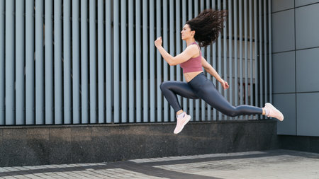 Sporty woman in active wear running fast and doing jumping exercise outside. Athlete female exercising outdoors. Cardio workout in street.の写真素材