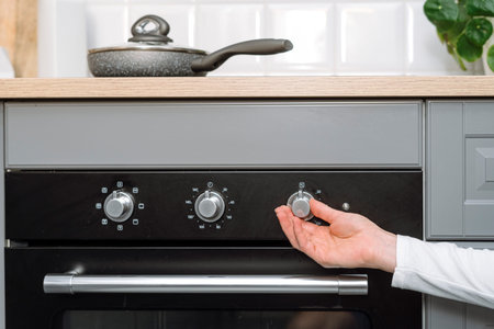 Closeup on female hand turn on electric oven on kitchen. Woman adjusting temperature mode using knob...