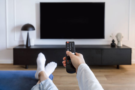 Selective focus on woman hand hold remote control and turn on tv panel on wall while relaxing on...