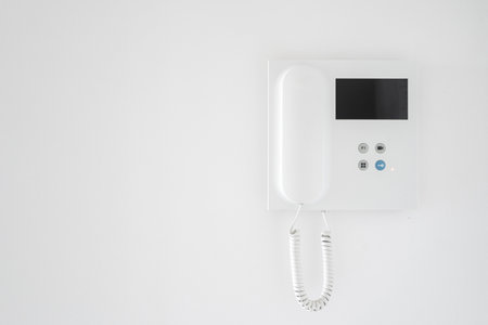 Modern intercom system with handset on white copy space wall in apartment hallway. Doorbell device with video monitoring and voice connection to unlock entrance. Control and security conceptの写真素材