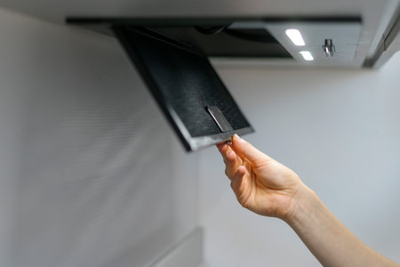 Woman removing black metal air filter from cooker hood for cleaning or service. Cropped shot of female hand change aluminum mesh in kitchen extractor. Maintenance household appliancesの写真素材