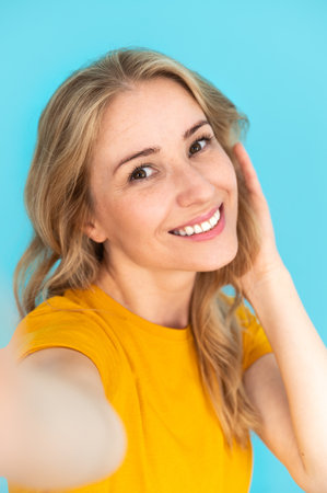 Vertical shot of happy smiling woman looking at camera and making selfie over blue background. Using smartphone for taking photo for social media, blog . Record video.の写真素材