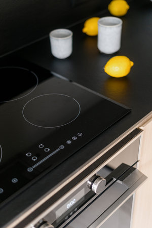 Closeup on glass ceramic induction stove with control panel, electric oven and ripe fresh lemons on black countertop at kitchen with modern interior. Household appliances at stylish apartmentの写真素材