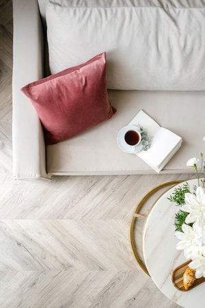 Top view on comfort couch with soft decorative pillow, open notebook and cup of tea in living room. Flat lay of marble coffee table with bloom flowers near sofa at cozy apartment.の写真素材
