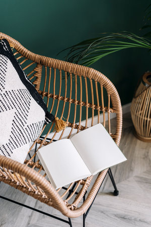 High angle view on open notebook with copy space on rattan armchair with decorative cushion. Stylish...