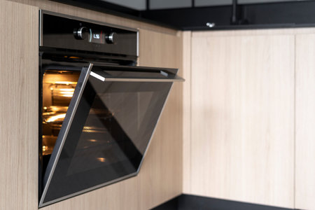 Empty electric oven with hot air ventilation and light inside. Open door in built in microwave....