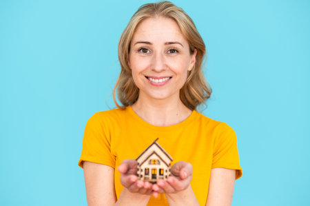 Real estate woman agent looking at camera and smiling on blue background. Advertising concept of house insurance. Female realtor offering property buying, rent of apartment, mortgage consultation.の写真素材