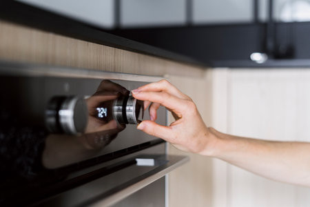 Close up view of woman hand regulate button, choosing microwave mode at modern oven with digital display and knobs on control panel. Housewife using household appliance on kitchen while cooking foodの写真素材