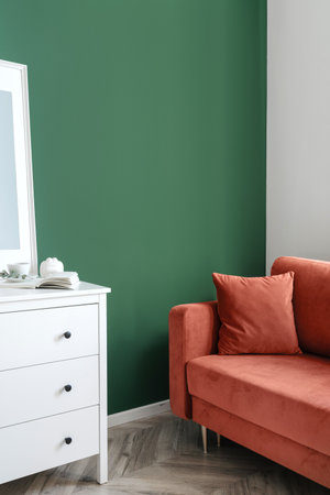 Vertical shot of classic interior design in living room with red couch, white elegant wooden commode against green wall with copy space. Place to rest in cozy homeの写真素材