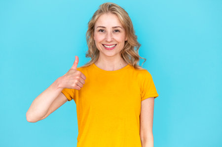 Happy woman showing thumb up gesture, standing isolated on blue copy space background. Student approving freelance work offer, looking at camera. Concept of agreement or deal signの写真素材