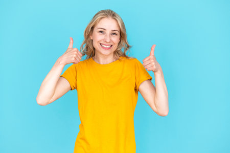 Excited smiling young woman in casual wear showing thumbs up isolated on blue background. Satisfied female making like gesture or recommending something. Happy, good choice or decision.の写真素材