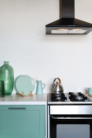Front view on gas stove with oven, blue cupboard with white countertop, cooker hood, clean plates,...