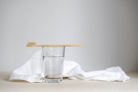 Wooden toothbrush on glass with drinking water, against cotton and fresh face towel. Morning routine at home, oral care, dental health concepts. Copy space backgroundsの写真素材
