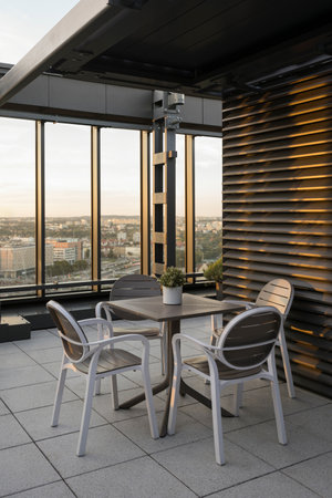Vertical shot of roof top cafe with cityscape view. Table and chairs on lounge terrace of high rise architecture building in city. Sunset light. Place for relax and restの写真素材