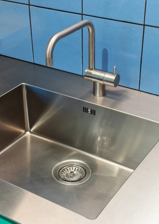 High angle view of empty and glossy stainless steel sink under metal chrome faucet in kitchen. Clean...