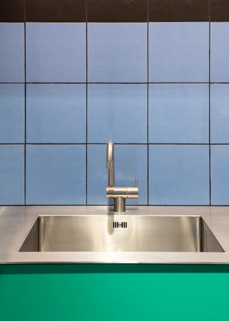 Colourful kitchen interior with metal sink and chrome faucet against blue wall tile in room. Glossy...