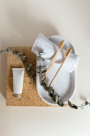 Flat lay top view of eco-friendly bamboo toothbrushes and eucalyptus leaf on stone tray with towels,...
