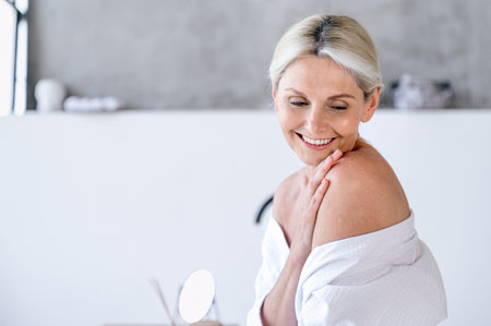 Smiling middle aged woman enjoy pure smooth skin, touching naked shoulder after beauty treatment procedures at home bathroom. Self care and bodycare conceptの写真素材