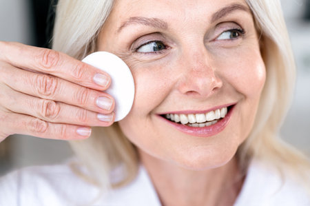 Close up portrait of happy mature woman wash up her perfect face, using cotton pads and cleansing product. Middle age lady removing makeup, applying rejuvenation products for skinの写真素材