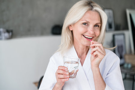 Deficiency prevention of vitamins. Mid age woman with toothy smile taking supplements at home. Multivitamin antioxidants for older female. Copy space.の写真素材