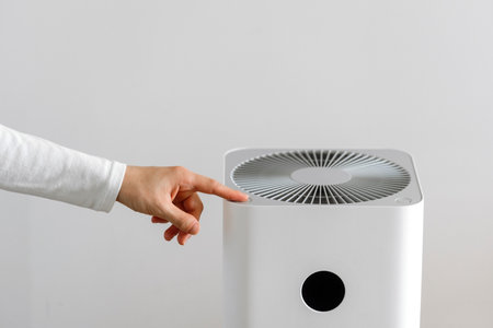 Cropped shot of woman hand pressing button on household air purifier on white background with copy space. Female using modern humidifier for moisture and ionizing at home. Climate control applianceの写真素材